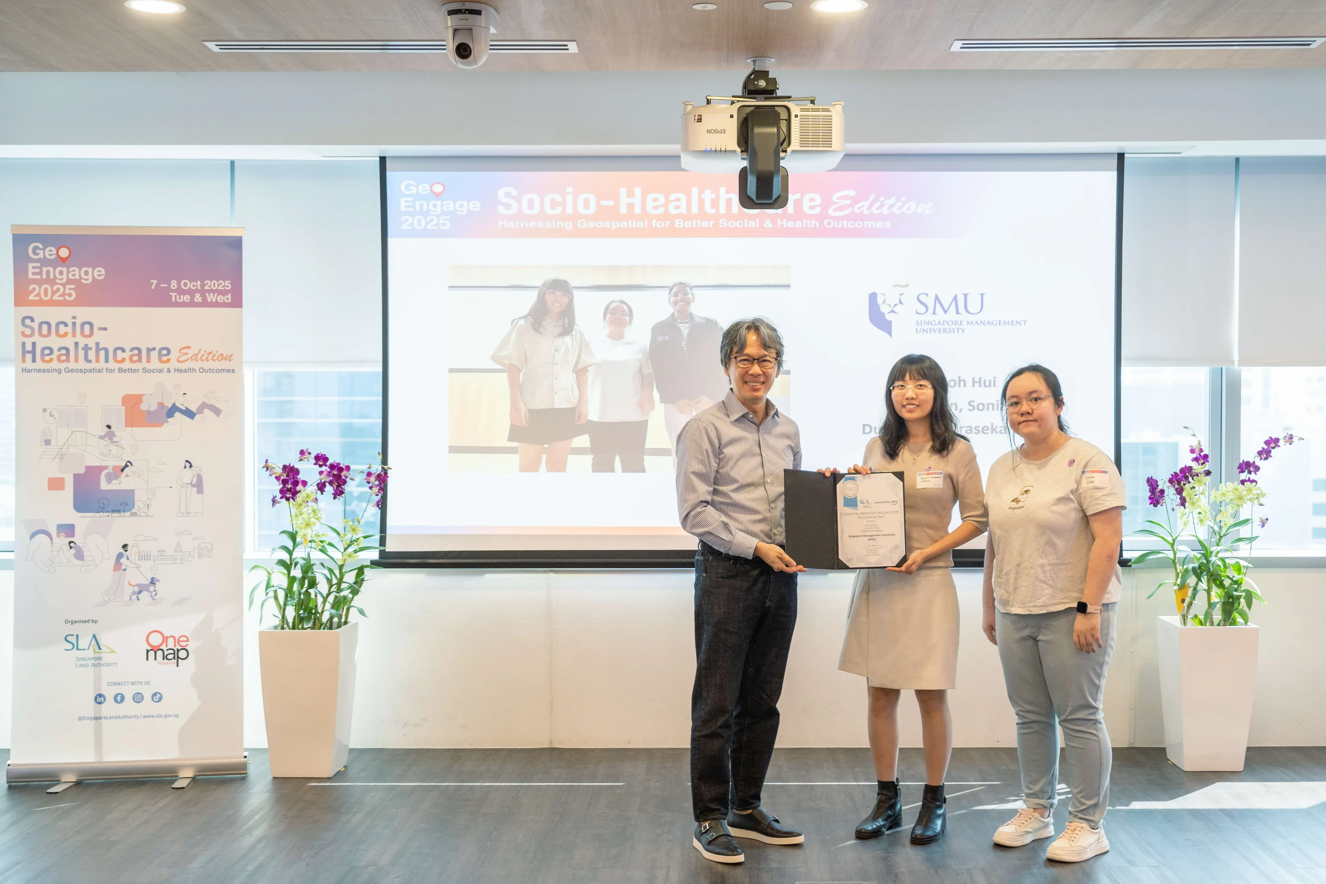 Three people stand together holding a certificate at the GeoEngage 2025 Socio-Healthcare Edition event.